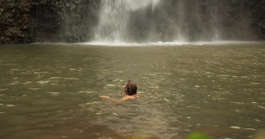 A man swims in the water by the waterfall