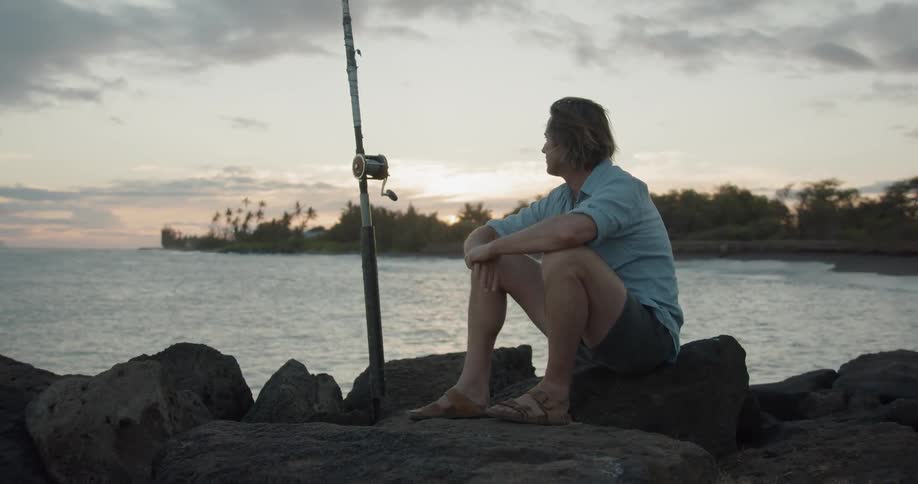 A man sits on the rocks with a fishing pole