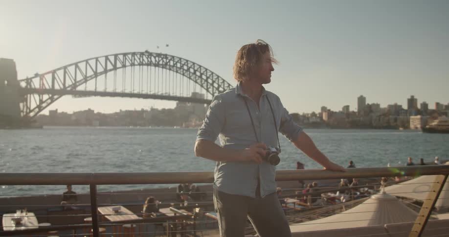 A man holds a camera outside by the water