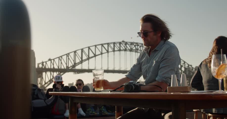 A man is drinking a beer at a table on a ferry outside in daylight