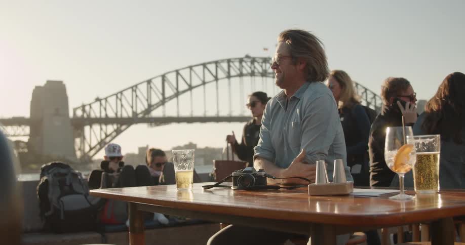 A man drinks beer at a table by the water