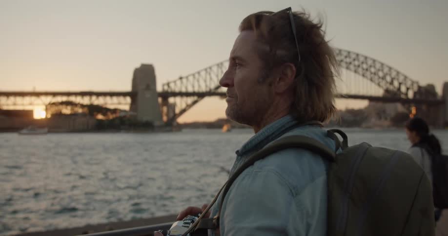A man holding a camera looks out at the water at sunset