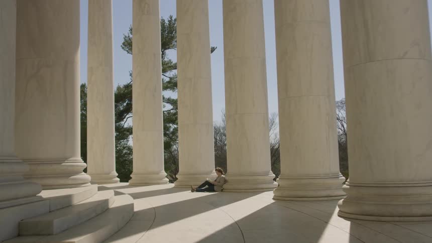 A woman sits leaning against a large marble pillar