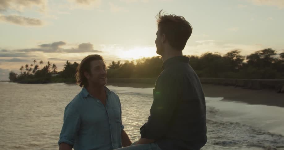 Two men talk on a beach at sunset
