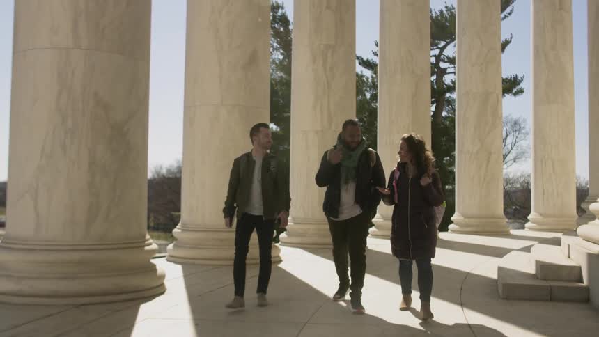 A group of people walking beside tall pillars in sunlight