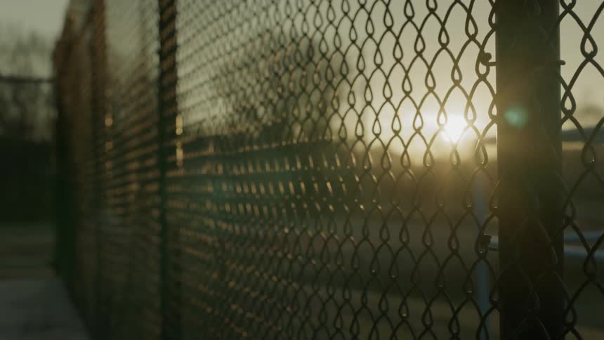 The sun shines through the links of a fence at sunset