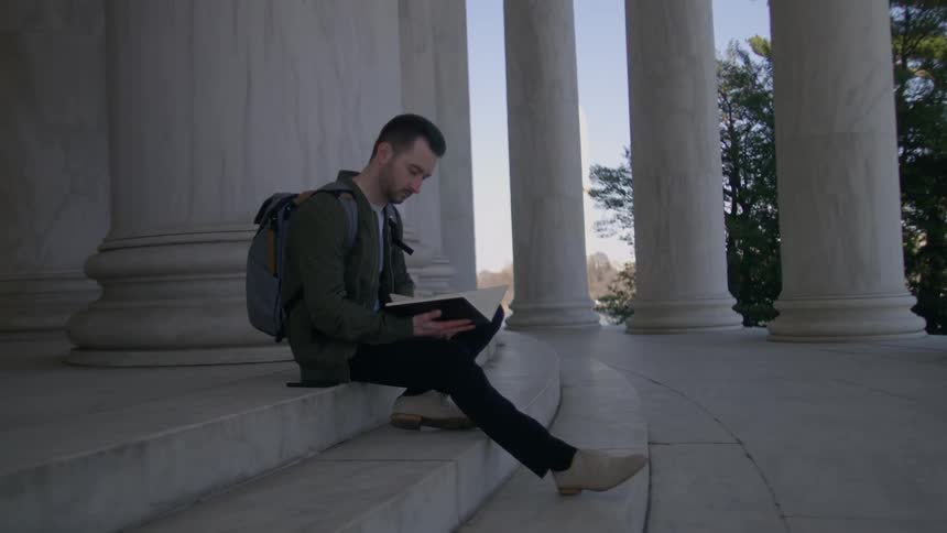 Man looks at a notebook while sitting on marble steps