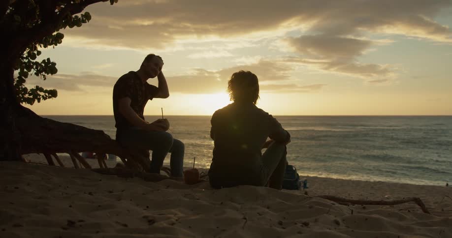 Two men talk on a beach at sunset