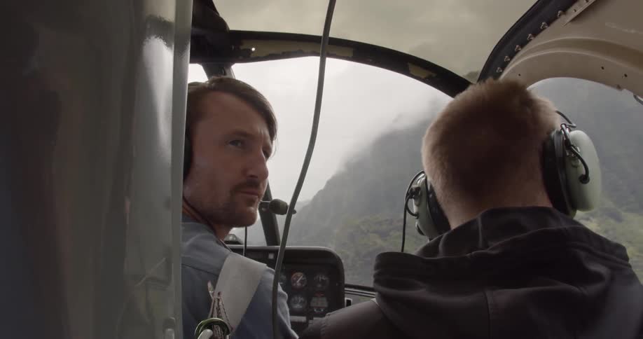 Two men are flying in helicopter by mountains