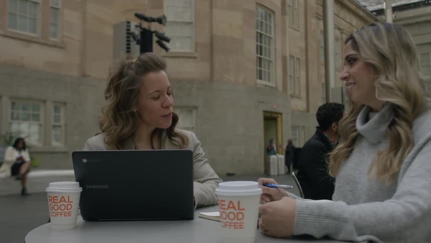 Two women talk and use a laptop outside