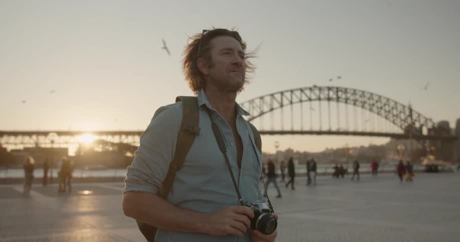 A man holds a camera outside by the bridge