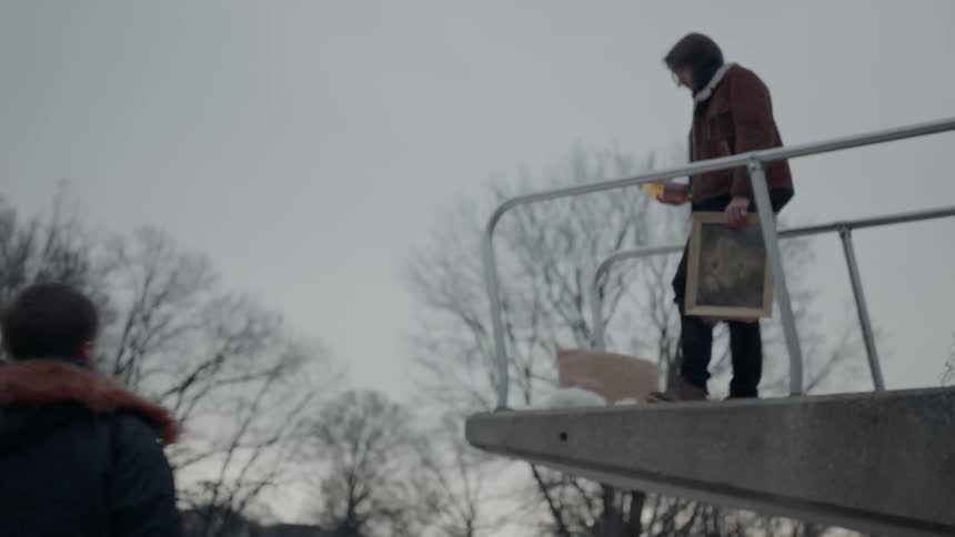 Man holds a photo on a diving platform as another man watches