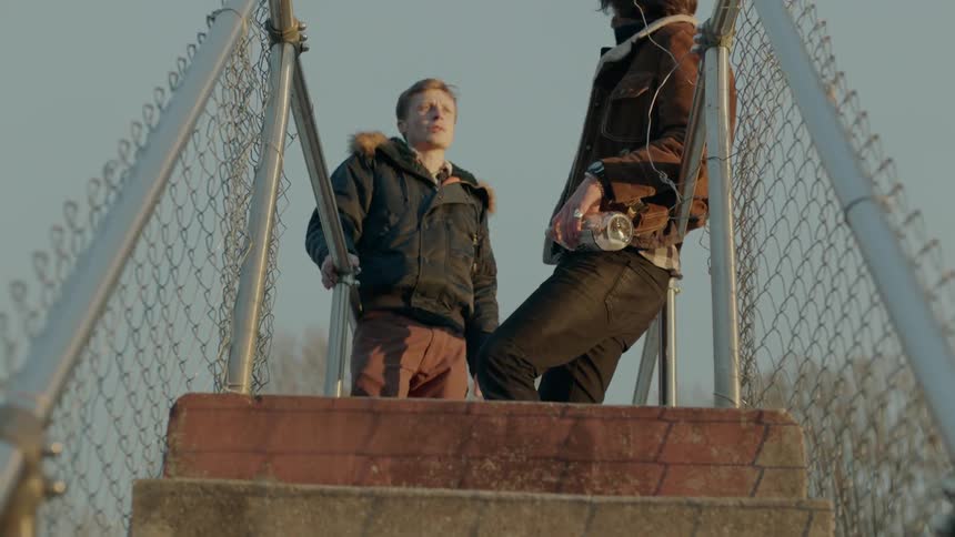 Two men talk while standing on a bridge