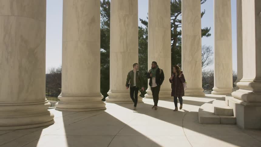 Three people walk by the large columns