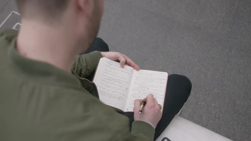 A man sits down writing in a notebook