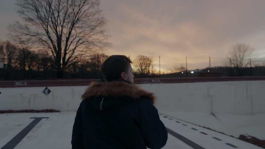 A man walks in an empty pool smoking a cigarette at sunset