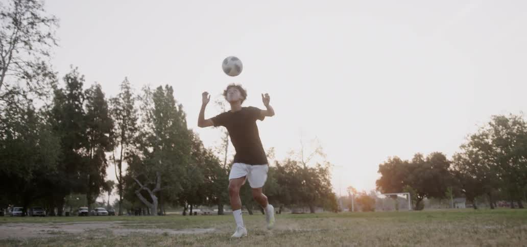A boy hits a soccer ball with his head then dribbles it