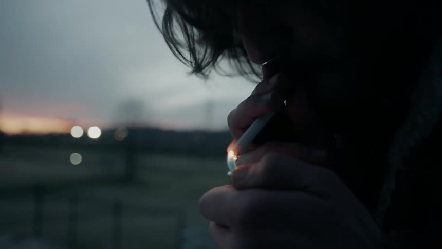 A man lights a cigarette at sunset