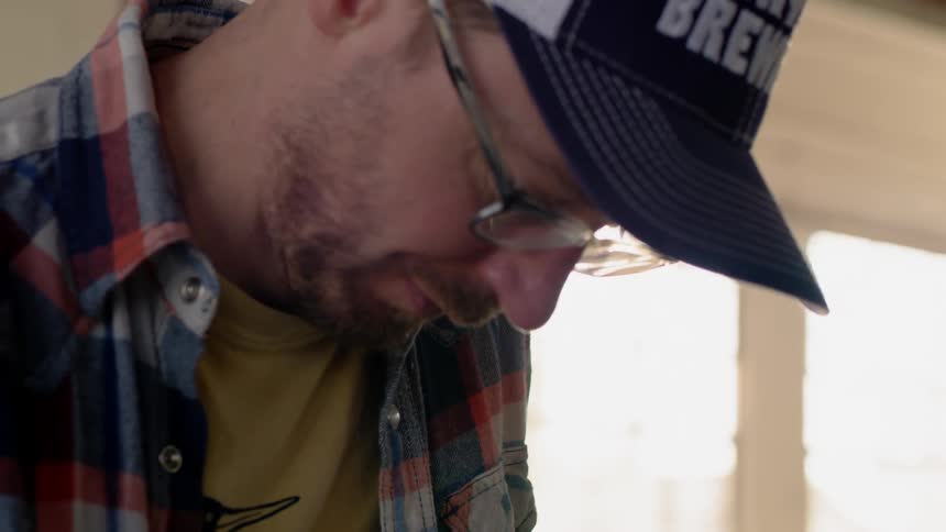 A man wearing a cap looks down while working on something