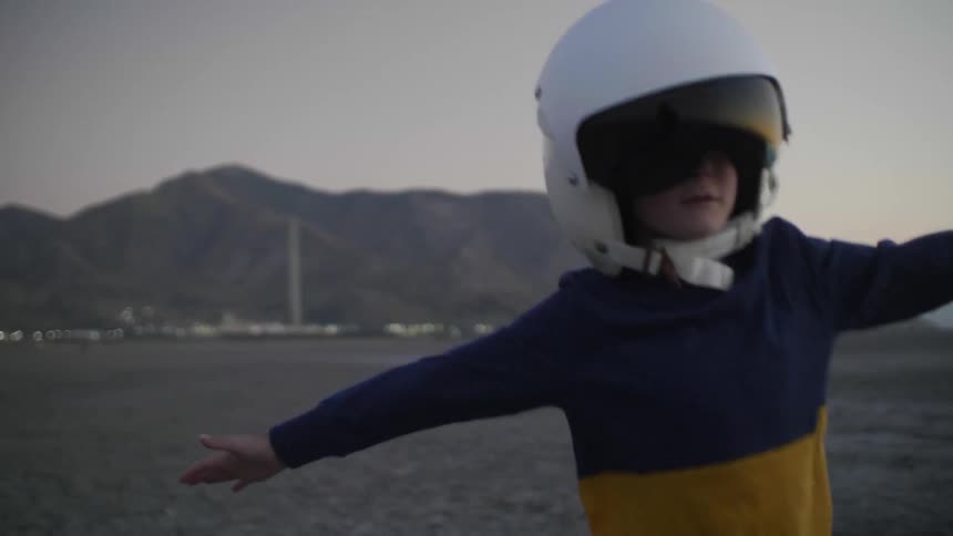 A young boy runs away with his arms out wide while wearing a helmet