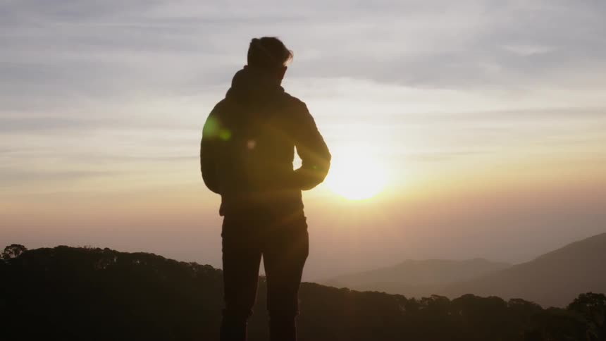 A man takes a photograph on the hill at sunset