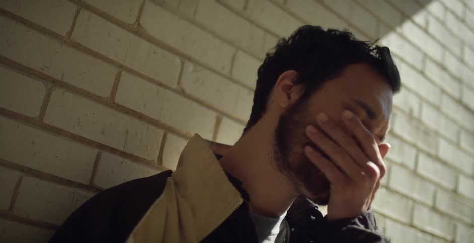 Man leans against wall and rubs chin