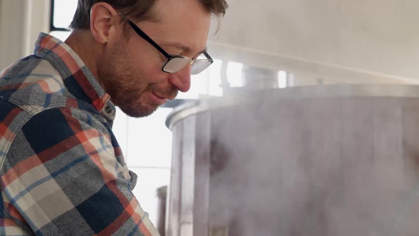 A man is working leaning over a steam covered container