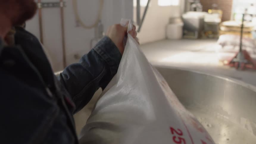 A man pours a large bag into a vat