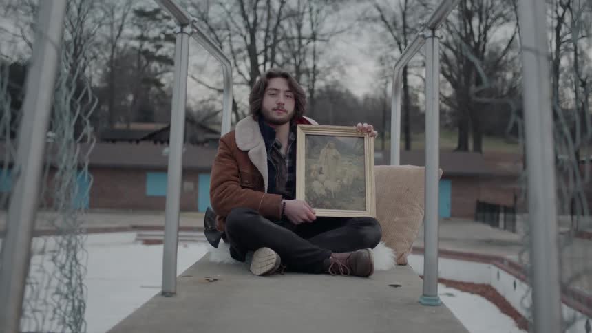 Man holds a framed photo as he sits on a platform