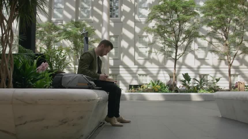 A man sits by a building writing in his book