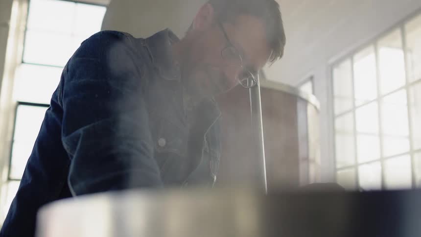 Man stands over a steaming vat in a factory