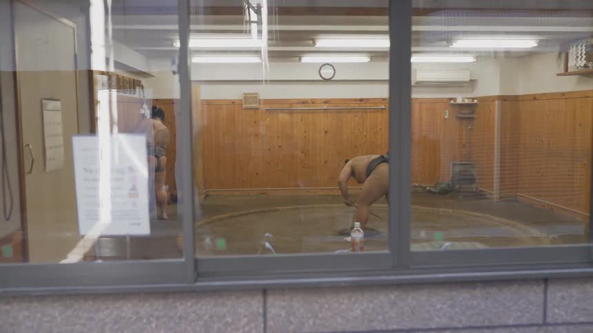 Two sumo wrestlers stand in a room