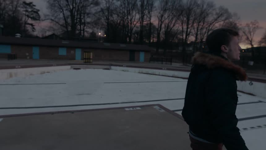 Man smokes next to an empty motel swimming pool at dusk
