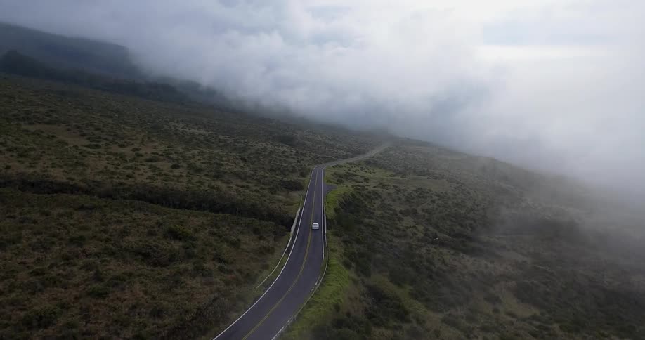 Clouds hover low over a mountain road a car is driving on