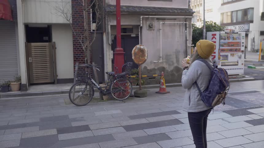 Person wearing a backpack stands in a city drinking out of a bottle