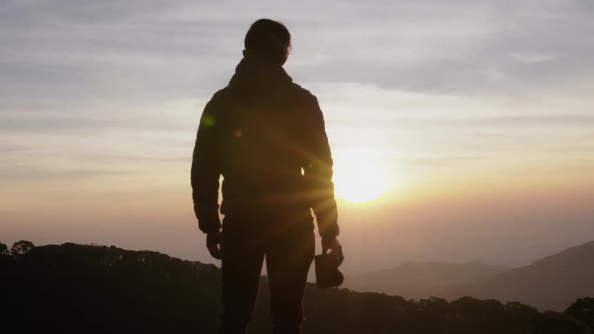 A man holds a camera atop the mountain