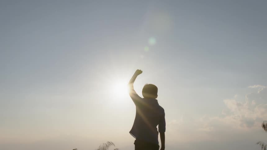 Young boy raises his arm as he stands under the bright sun