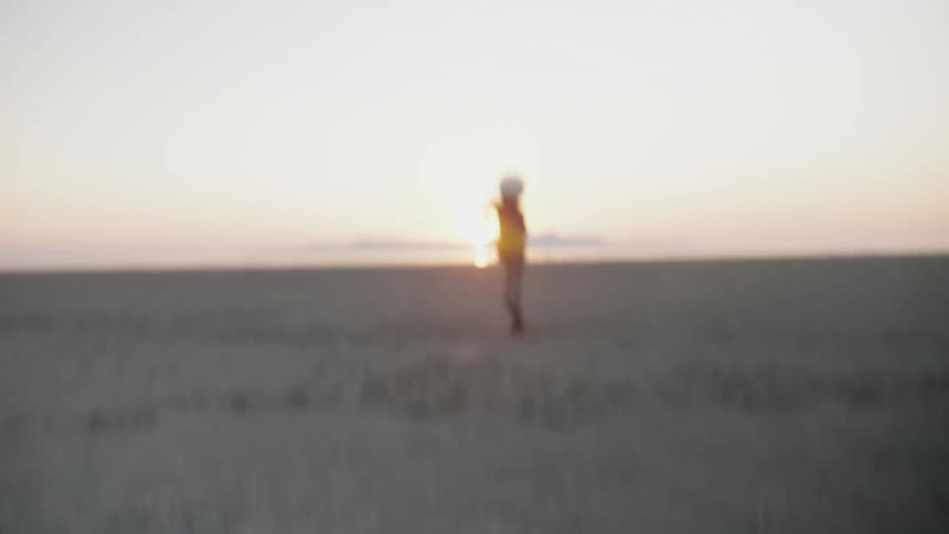 A boy in a helmet runs fast across the sand as the sun sets