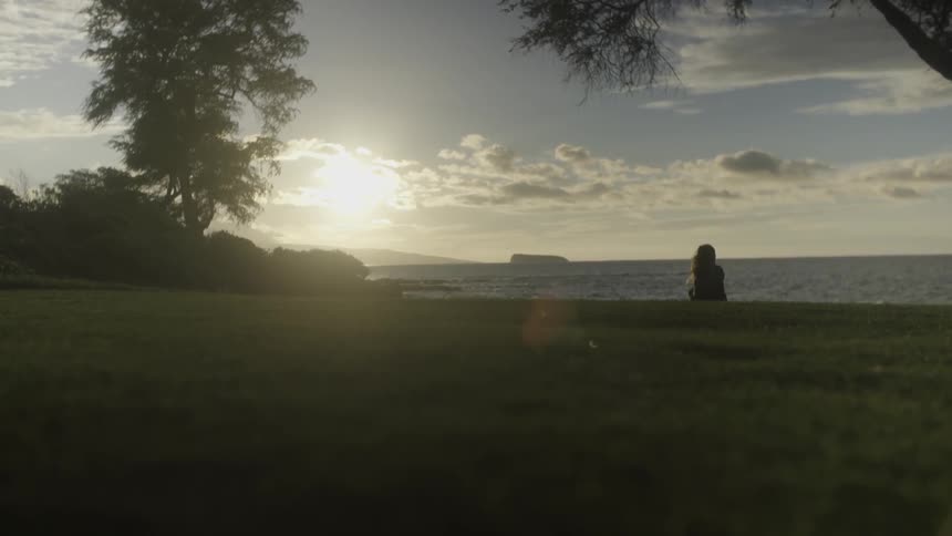 A young woman sits on the shoreline as the sun shines