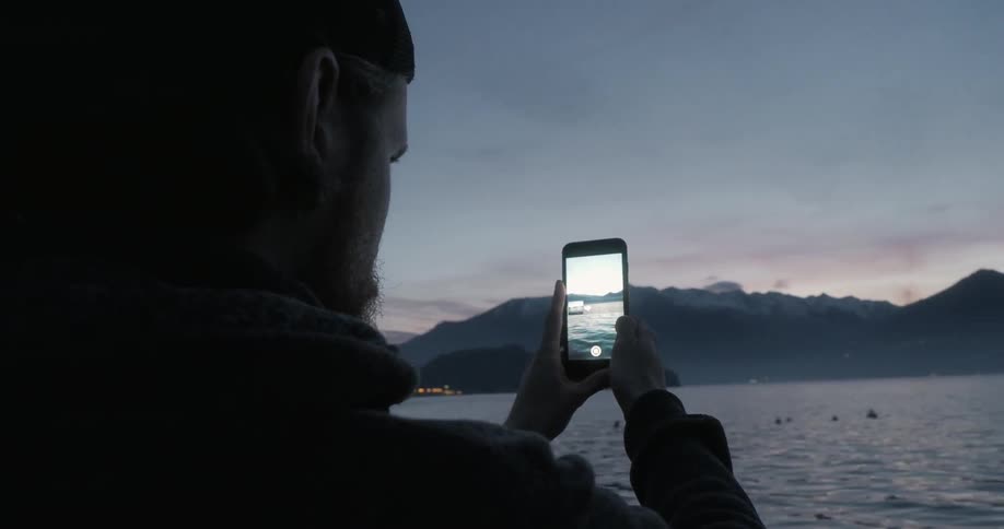 A man is using his cellphone to film a bay at night