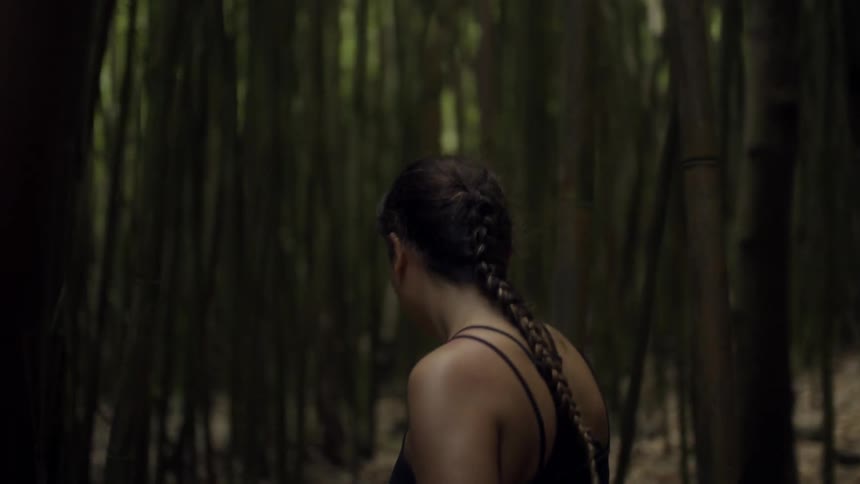 A woman is hiking through a dense forest of bamboo