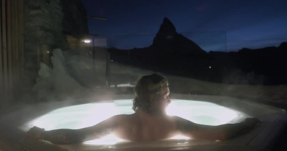 A man stretches out in an outdoor hot-tub at night