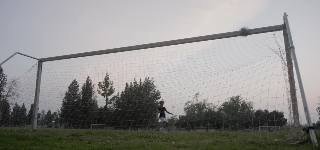 A boy kicks a goal with a soccer ball