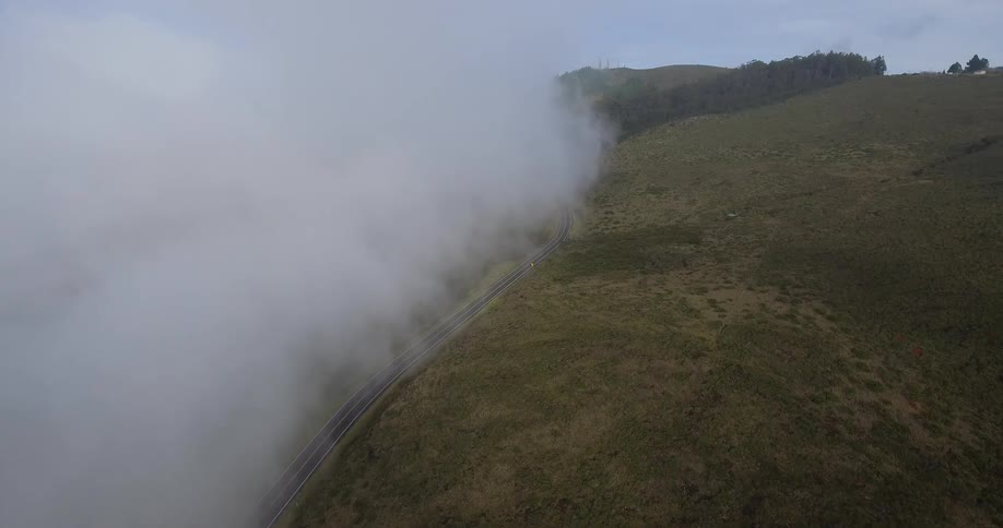 Clouds are partially covering a road on a hilltop
