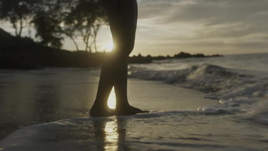 A person stands on the beach as waves roll on their feet