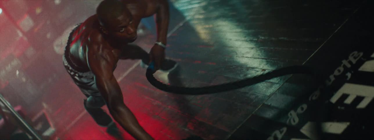 A man whips around a rope in the gym then jumps up to pull them