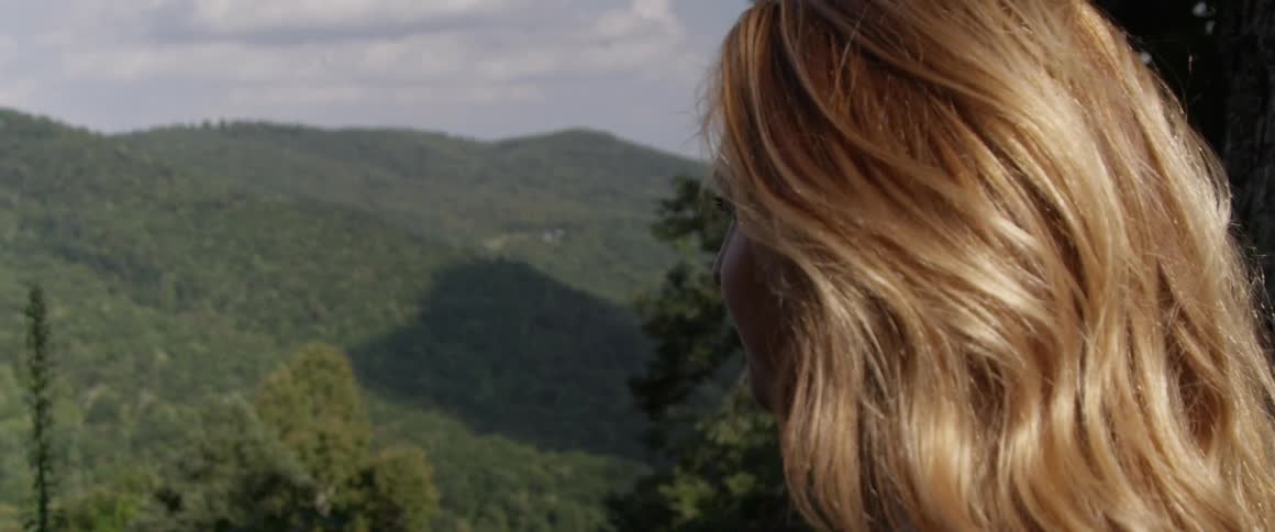 A young woman stands a looks out at the tree-covered mountain range
