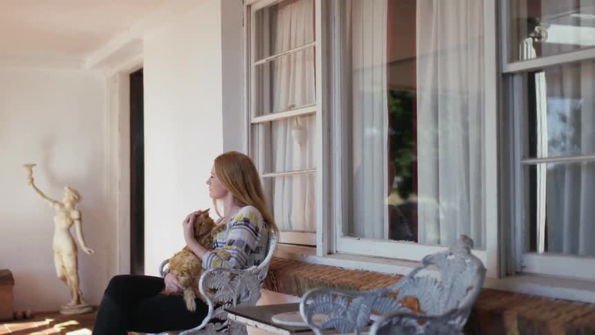 Woman nuzzles a cat as she sits on a porch