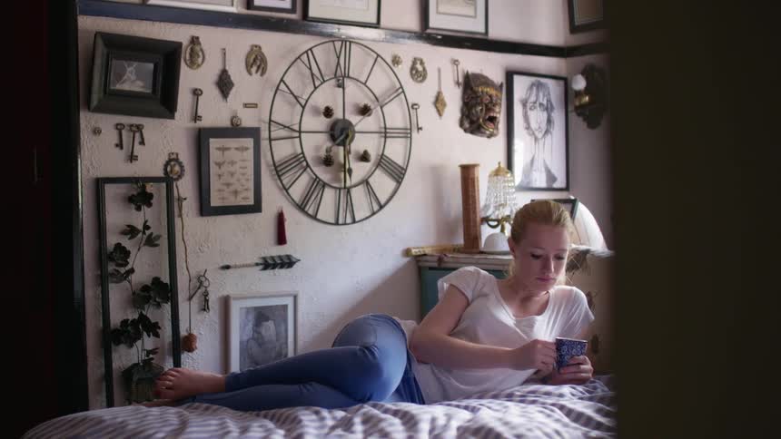 A woman drinks from a mug while lying in bed