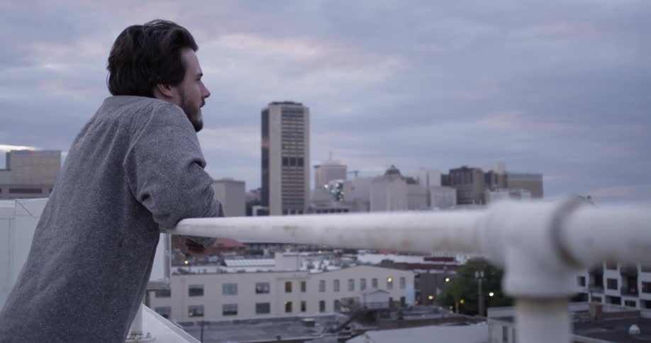 A man leans over a rail on a rooftop